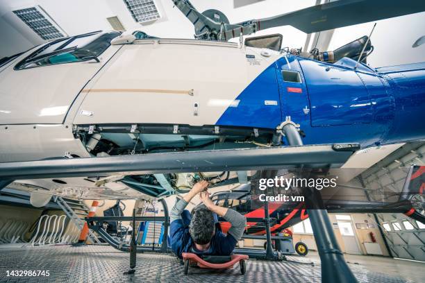aviation engineer lying on cart on wheels and fixing helicopter engine, back view - jet lag stockfoto's en -beelden