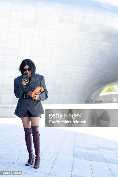 Guest wears a grey jacket with black shorts, a burnt orange bag, plum knee-high boots and a black belt outside Dongdaemun Design Plaza at Seoul...