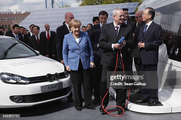 German Chancellor Angela Merkel and Chinese Premier Wen Jiabao look on as Volkswagen CEO Martin Winterkorn holds a cable to polug in a Volkswagen...