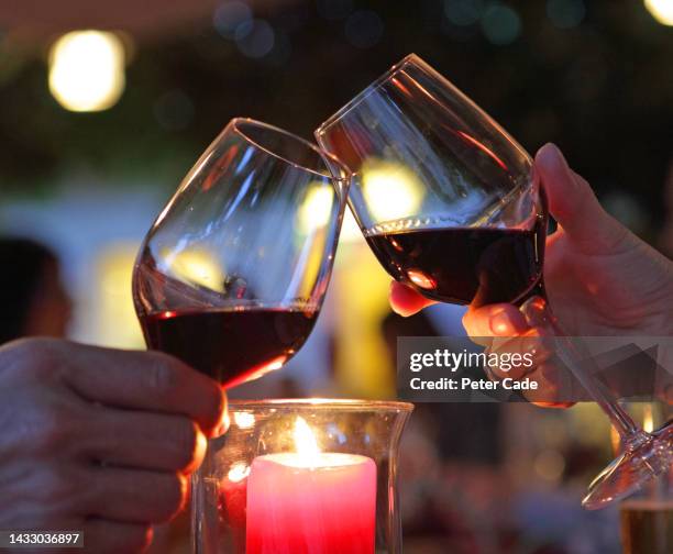 couple clinking glasses of red wine in candlelit restaurant - young couple date night wine stock pictures, royalty-free photos & images