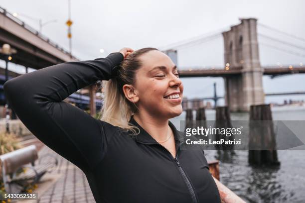 mujer joven arreglando el cabello antes de correr en nueva york - new sport content fotografías e imágenes de stock