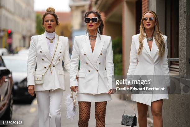 Guest wears a gold large chain pendant necklace from Dior, a white ruffled high neck / top, a white latte blazer jacket, a white shiny leather...