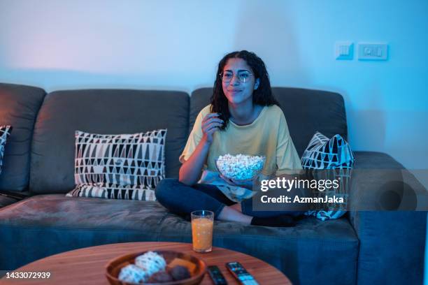 young hispanic female enjoys her evening at home. she sits in her living room and watches tv - one kid one world a night of 18 laughs stockfoto's en -beelden