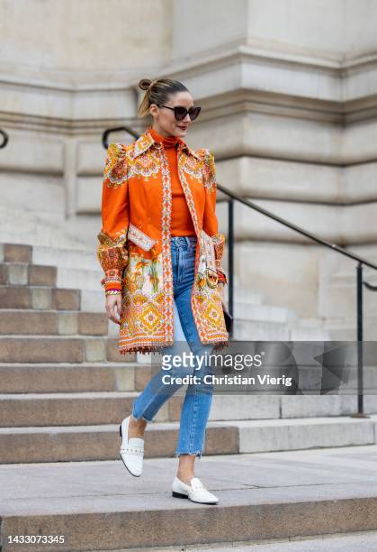 Olivia Palermo wears orange strong shoulder line jacket with floral print, turtleneck, denim jeans, white loafers, sunglasses outside Zimmermann...