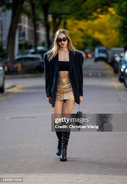 Georgina Gigi wears golden glitter skirt, black cropped top, oversized blazer, bag, knee high black boots on October 12, 2022 in Amsterdam,...
