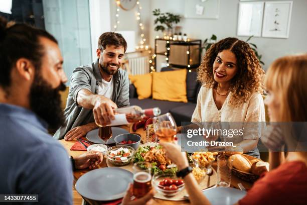 friends and family eating dinner and drinking wine. man opening wine bottle and pouring to guests - opening night dinner stockfoto's en -beelden