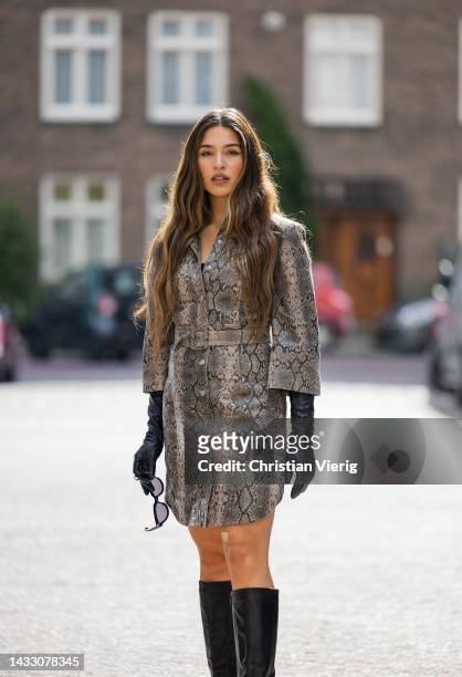 Isaya Elias wears dress with snake print, black gloves, knee high boots on October 12, 2022 in Amsterdam, Netherlands.