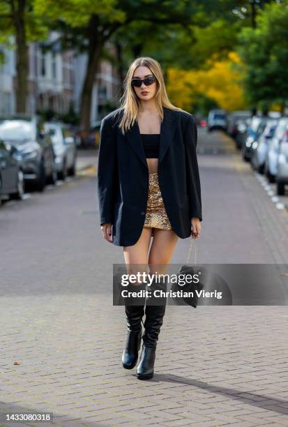 Georgina Gigi wears golden glitter skirt, black cropped top, oversized blazer, bag, knee high black boots on October 12, 2022 in Amsterdam,...