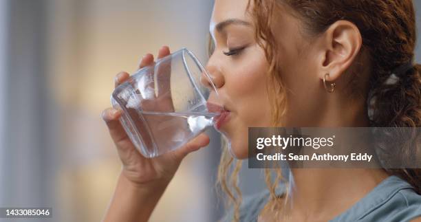 closeup of a woman drinking a glass of water for hydration, thirst and health at her house. happy girl with a wellness, diet and healthy lifestyle enjoying a fresh aqua drink while relaxing at home. - cup of water stockfoto's en -beelden