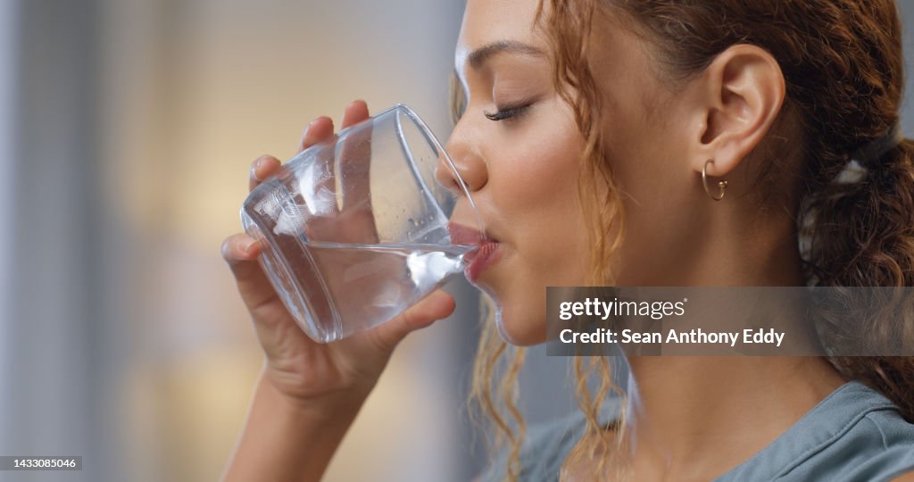 Closeup of a woman drinking a glass of water for hydration, thirst and health at her house. Happy girl with a wellness, diet and healthy lifestyle enjoying a fresh aqua drink while relaxing at home.