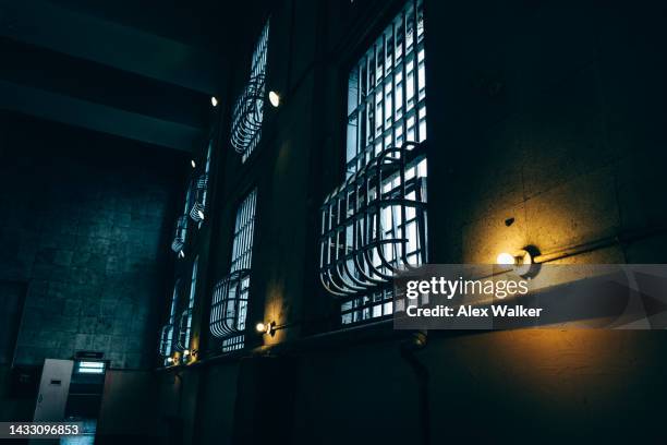 light bulb in darkened room with bars on windows - death row stock pictures, royalty-free photos & images