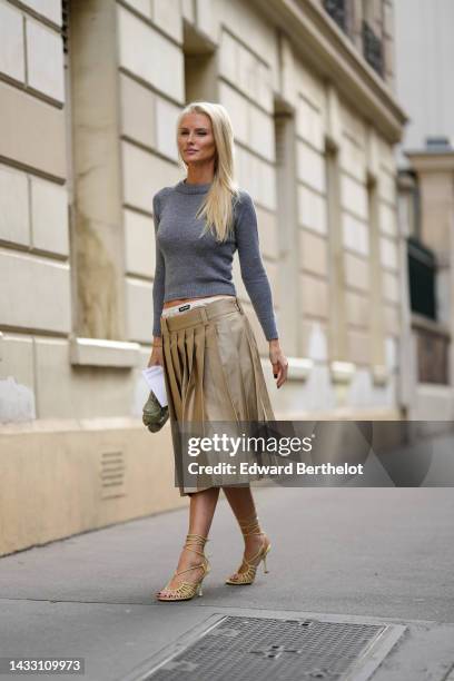 Guest wears a pale gray wool pullover, a beige pleated / accordion midi skirt from Miu Miu, pale yellow shiny leather strappy heels sandals, a khaki...