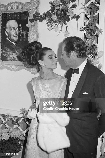 British actors Audrey Hepburn and Rex Harrison holding hands and smiling at each other at the Los Angeles premiere of their film 'My Fair Lady' in...