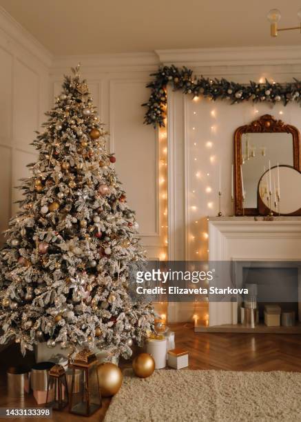 christmas concept. festive christmas rich interior in a luxurious modern style with a fireplace and decorated with christmas balls and garlands of christmas trees in a large bright living room in the apartment on new year's eve in winter. place for text - decorar fotografías e imágenes de stock