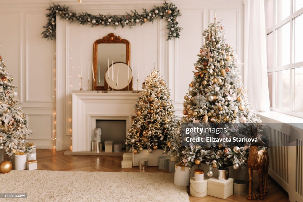 Christmas concept. Festive Christmas rich interior in a luxurious modern style with a fireplace and decorated with Christmas balls and garlands of Christmas trees in a large bright living room in the apartment on New Year's Eve in winter. Place for text