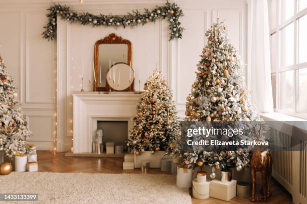 christmas concept. festive christmas rich interior in a luxurious modern style with a fireplace and decorated with christmas balls and garlands of christmas trees in a large bright living room in the apartment on new year's eve in winter. place for text - christmas tree living room stock pictures, royalty-free photos & images