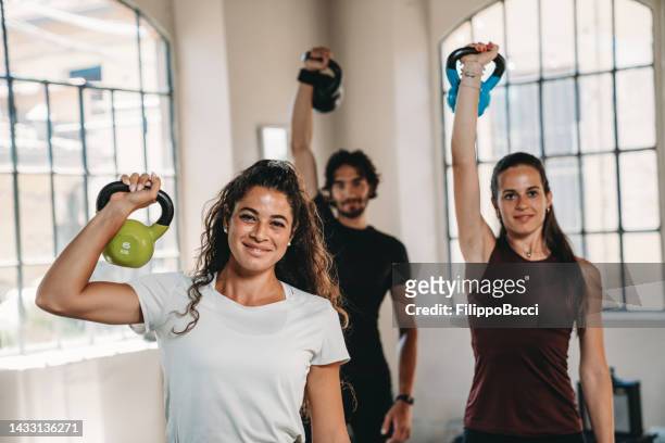 three people at the health club are training together - kettlebell stockfoto's en -beelden