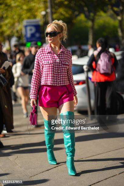 Guest wears black denim sunglasses from Prada, a white / neon pink houndstooth print pattern buttoned jacket, neon pink shiny satin shorts, a neon...