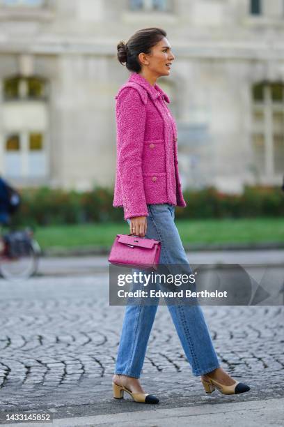 Guest wears crystal flower earrings, a pink fluffy jacket from Chanel, blue denim pants, a pink shiny leather ostrich shiny leather Kelly handbag...