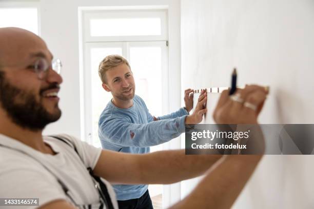 zwei männliche freunde, die mit einem maßband messen - room mates male stock-fotos und bilder