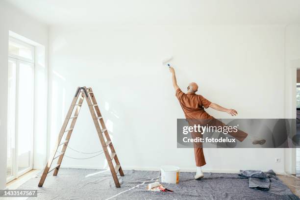 joven divirtiéndose mientras pinta la pared de su nueva casa - pared casa fotografías e imágenes de stock