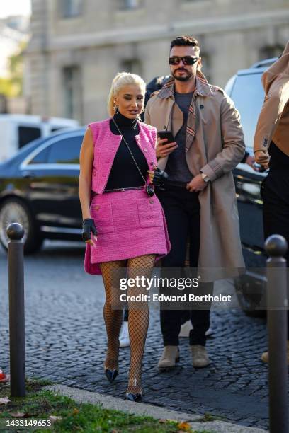 Guest wears silver and logo earrings from Chanel, a black turtleneck pullover, a pink tweed sleeveless jacket from Chanel, a pink tweed short skirt...