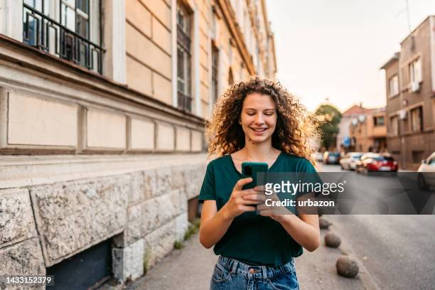 young woman using phone while walking down the street - portrait looking down stock pictures, royalty-free photos & images