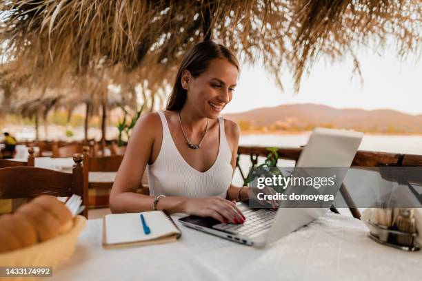 woman learning and using a laptop in a restaurant at the seaside - business studies stockfoto's en -beelden