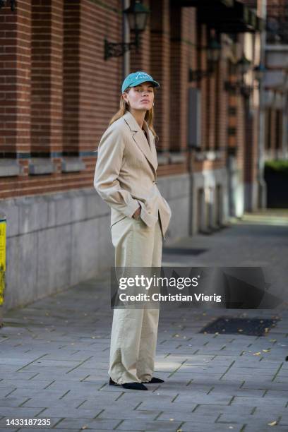 Lois Schindeler wears beige blazer, pants, black bag, cap, pointed heels wears on October 13, 2022 in Amsterdam, Netherlands.