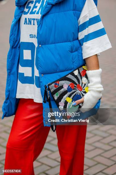 Talissa Benamou wears red pants, football shirt jersey with print, blue puffer vest, creme white gloves, clutch with print, Converse shoes on October...