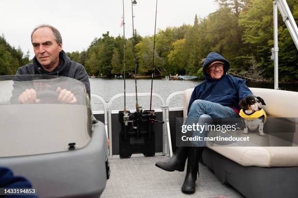 two senior men enjoying a pontoon boat tour on a lake in autumn. - pontoon boat stock pictures, royalty-free photos & images