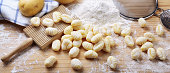 Uncooked potato gnocchi, with flour, sieve and gnocchi board on wooden pastry board, close-up.