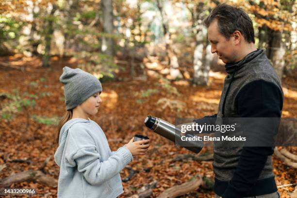 dad pours hot tea from a thermos with his daughter while walking in the autumn forest - flask stock pictures, royalty-free photos & images