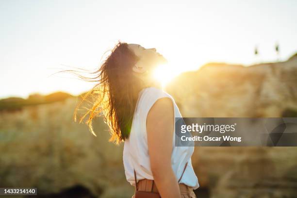 young woman head ups with eye closed against beautfiul sunset - japanese woman looking up stock-fotos und bilder