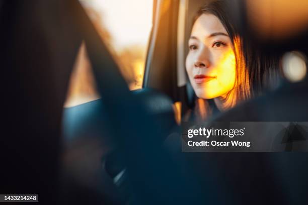 young asian woman looking through window in a car at sunset - car interior sunset stockfoto's en -beelden