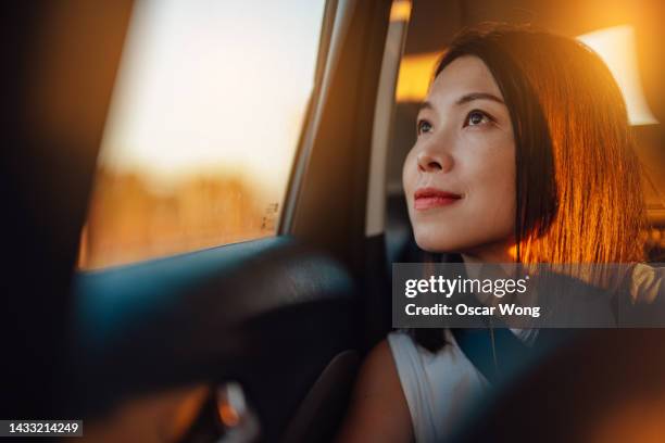 young asian woman looking through window in a car at sunset - car interior sunset stockfoto's en -beelden