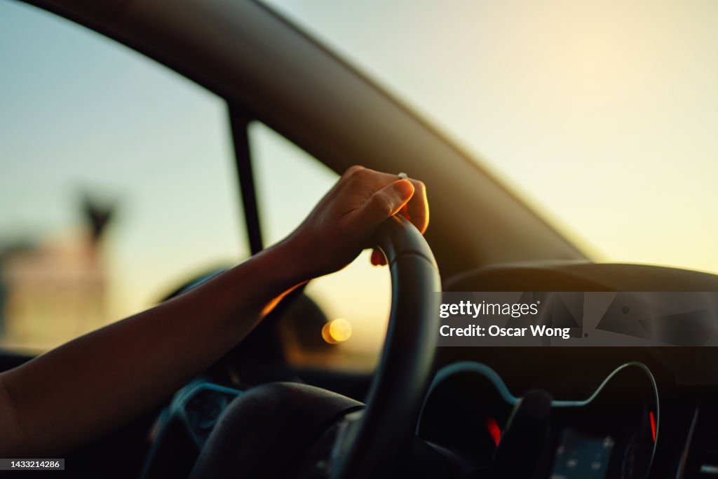 Female hand holding steering wheel in a car during a drive at sunset