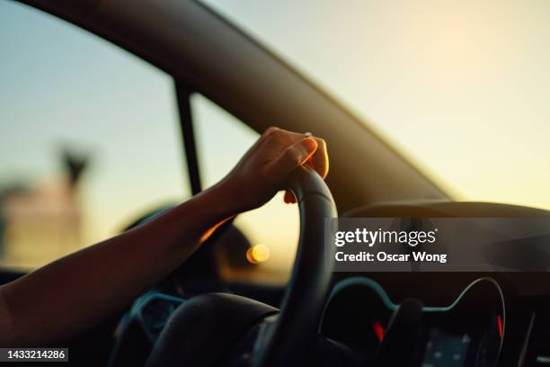 female hand holding steering wheel in a car during a drive at sunset - driver ストックフォトと画像