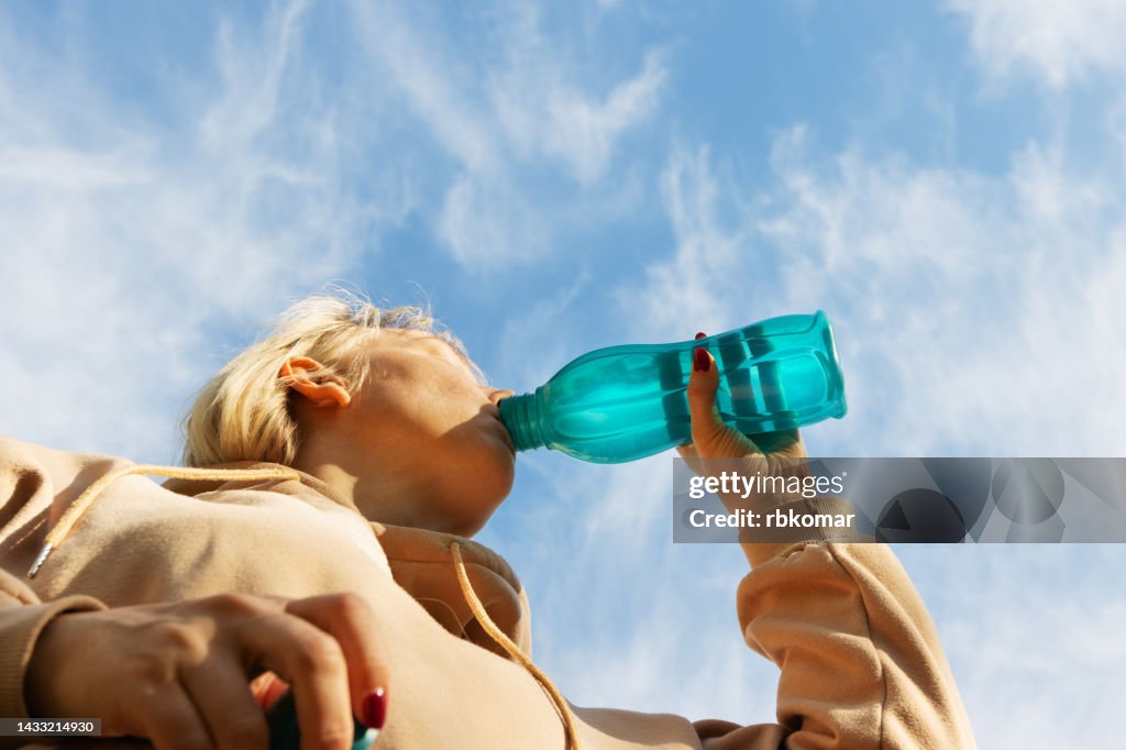 Woman drinking water while exercising outdoors on a sunny clear day