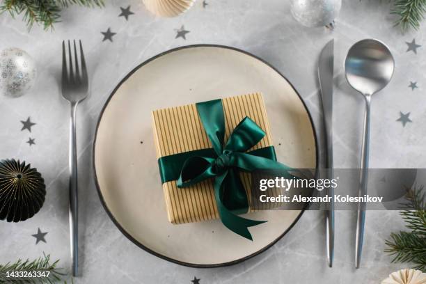 new year christmas present wrapped green ribbon on plate with silver cutlery on marble table. flat lay composition - box white flat stock-fotos und bilder