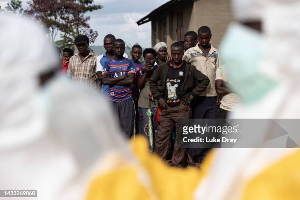 Villagers look on as Red Cross workers don PPE prior to burying a 3-year-old boy suspected of dying from Ebola on October 13, 2022 in Mubende,...