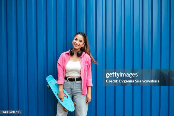 street portrait of a beautiful young woman with scateboard. - pink shirt stock-fotos und bilder