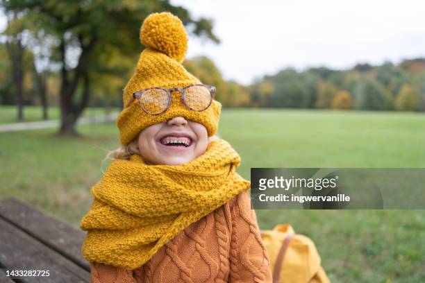 laughing girl covering her face with knitted hat in a park - girl scarf stock pictures, royalty-free photos & images