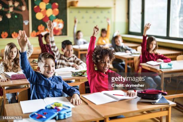 studenti elementari felici alzano le mani su una classe a scuola. - classroom foto e immagini stock