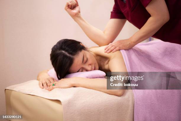 a female masseuse is massaging the back of a female patient. - body massage japan stock pictures, royalty-free photos & images