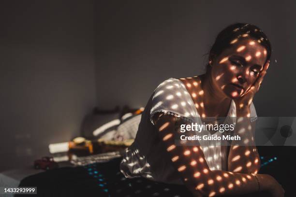 depressed woman sitting on a bed in darkend room. - depressie landelement stockfoto's en -beelden