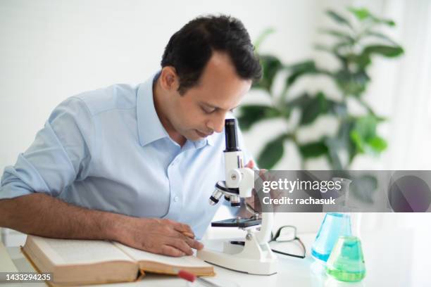 indian man looking in microscope - indian education health science and technology stockfoto's en -beelden