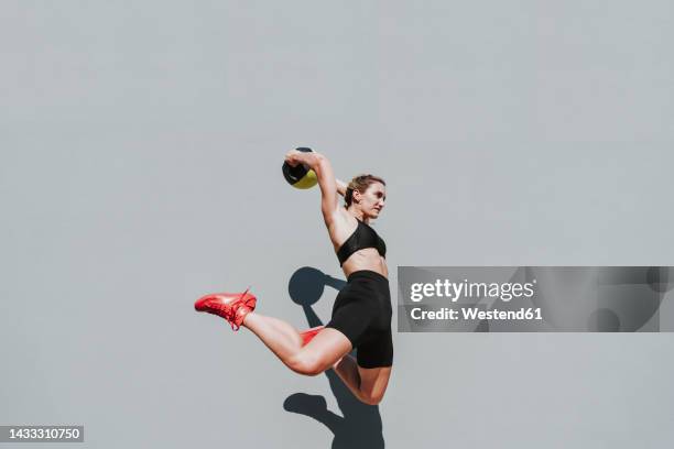 woman with medicine ball jumping in front of gray wall - medicine ball stock pictures, royalty-free photos & images