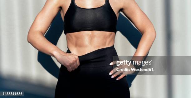 young athlete with hand on hip standing in front of gray wall - bauchmuskeln stock-fotos und bilder