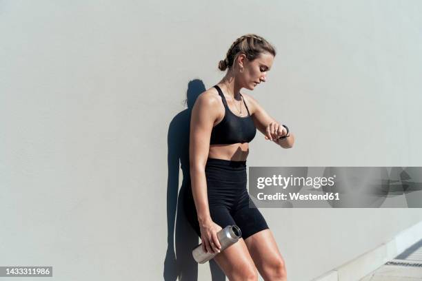 woman checking time leaning on gray wall - fitnesstracker stock pictures, royalty-free photos & images